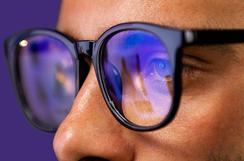 A person wearing glasses stares intently at a computer screen
