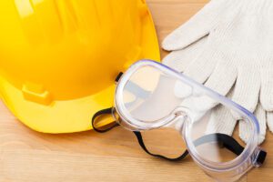 An image of a yellow hard hat, clear eye goggles, and white gloves.